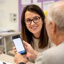 Maryfrances Pocius, friendly female tech instructor with glasses, demonstrating a smartphone to a senior student