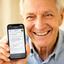 Charley Dolata, retired teacher beaming at camera, holding a smartphone showing a WhatsApp chat